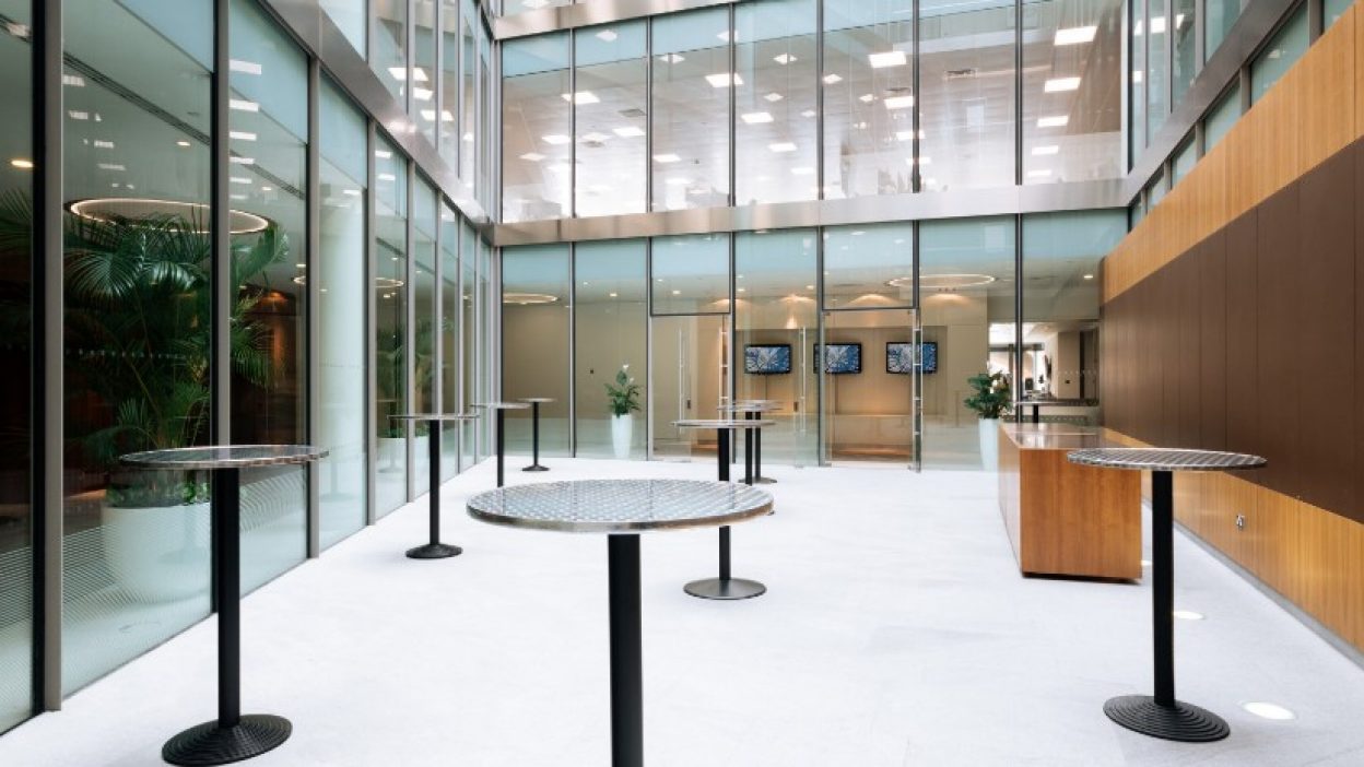 Atrium set for a drinks reception with tall bar tables and three branding screens in the background